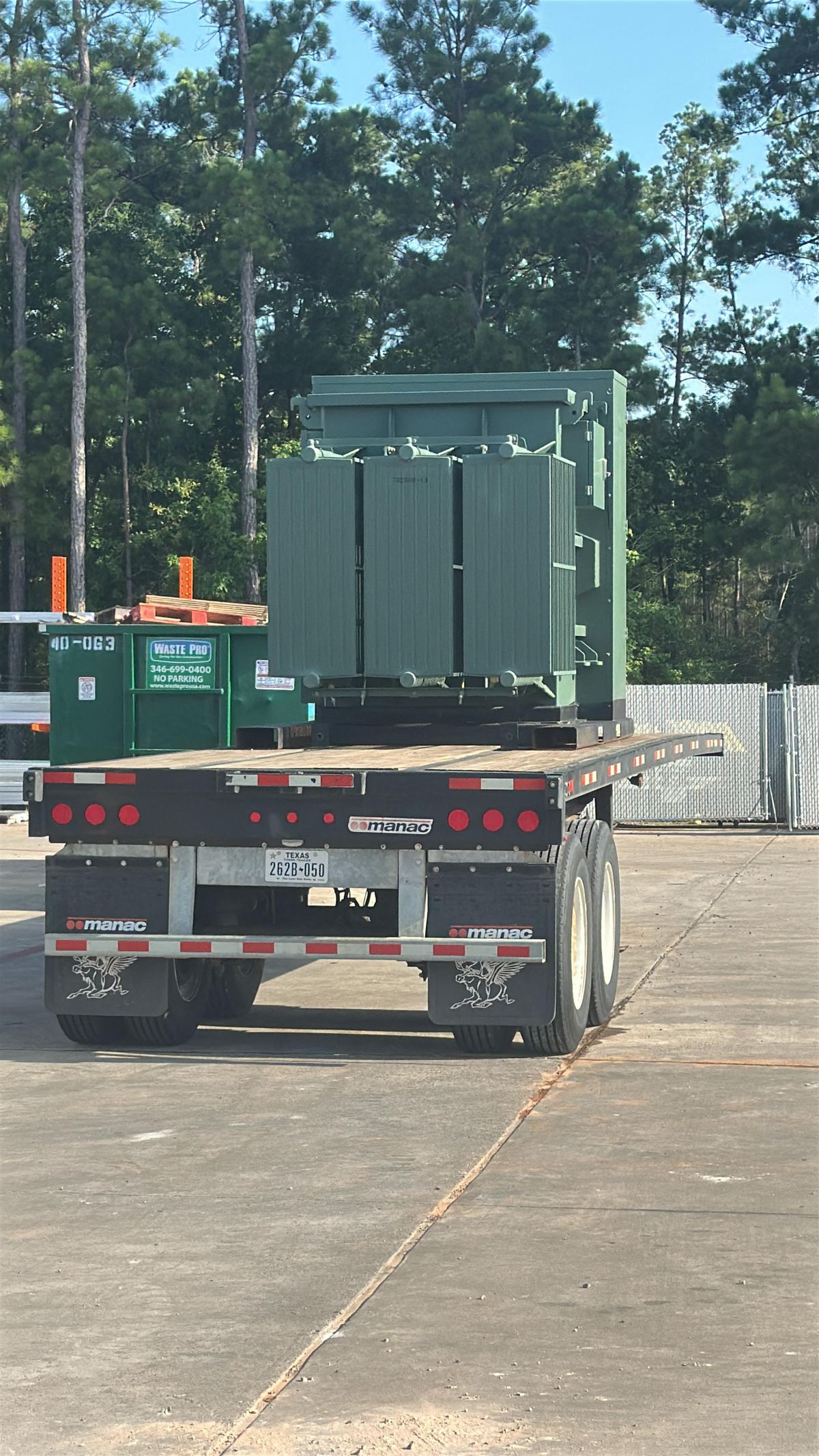 A large green electrical transformer strapped down on a flatbed trailer