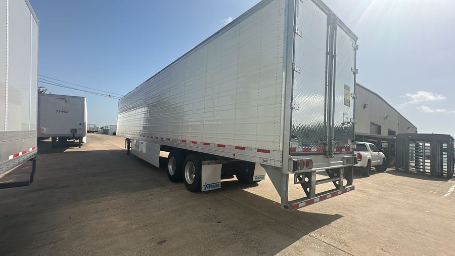 A clean white dry van trailer parked in the yard under a blue sky