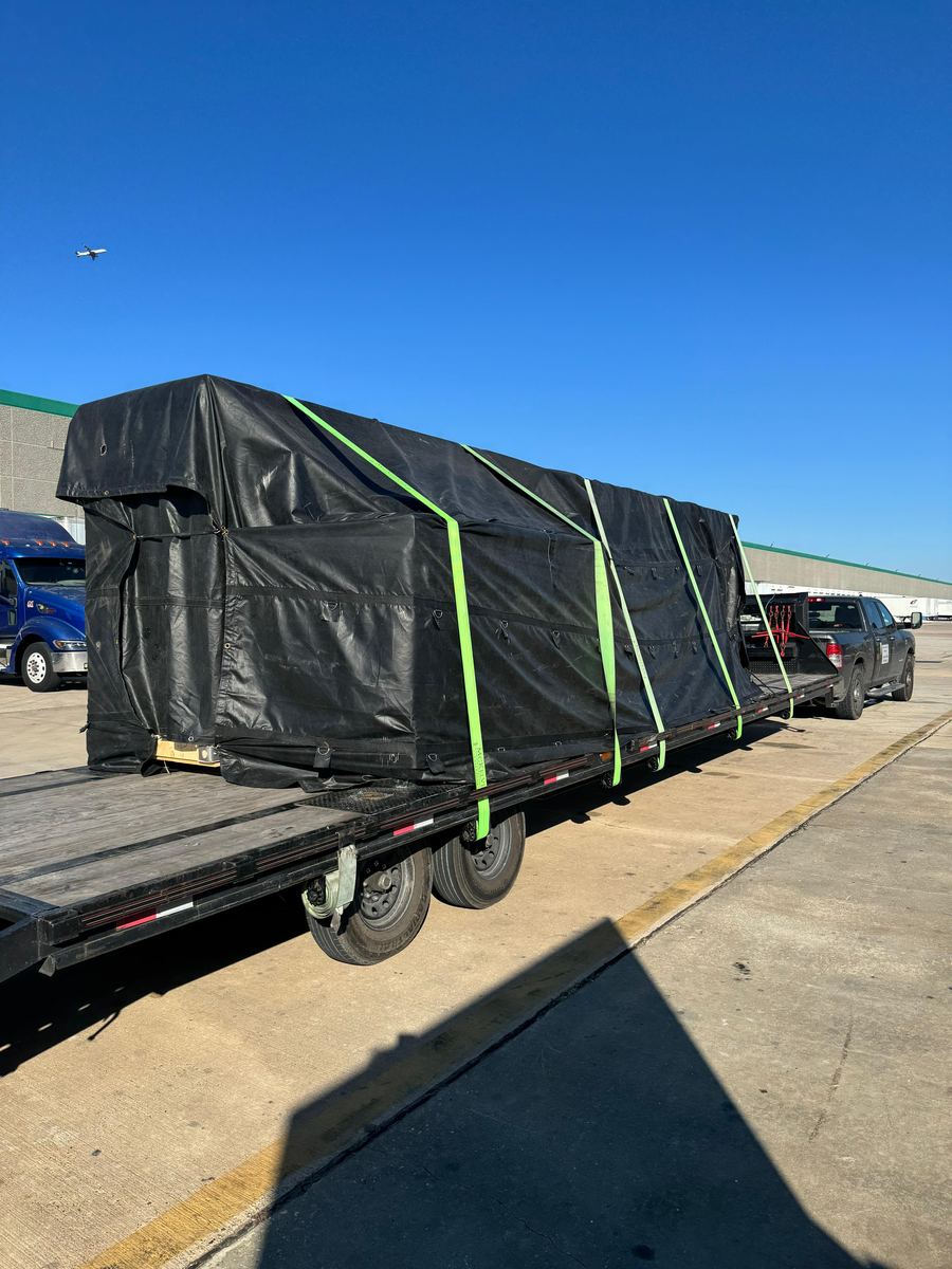 A long black-tarped load secured with green straps on a flatbed