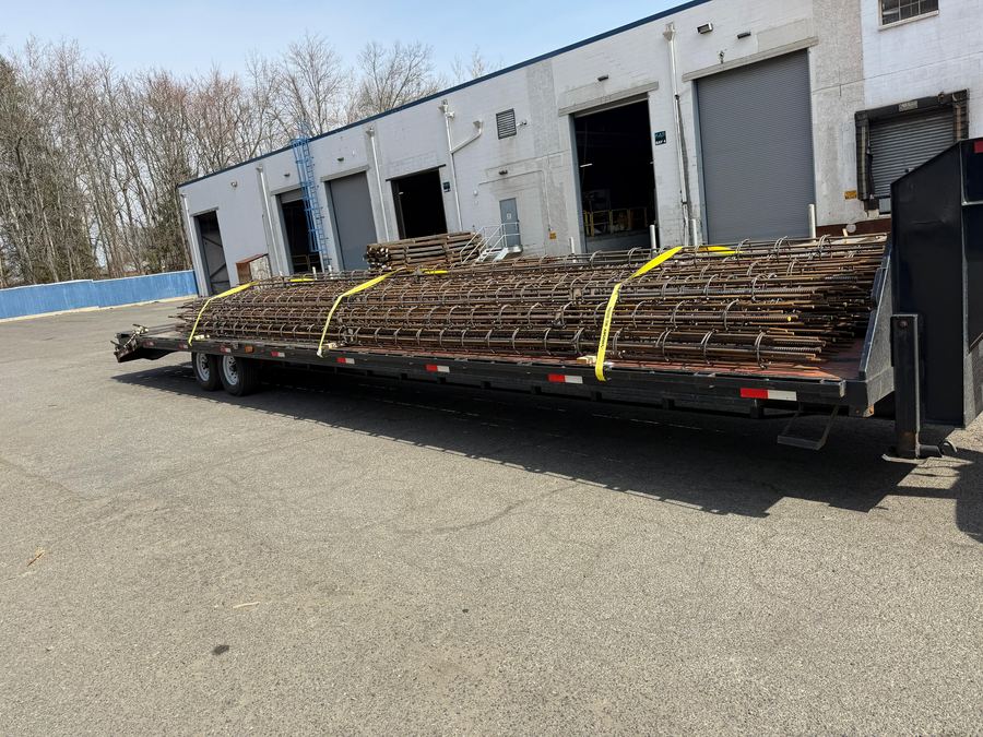 Bundled steel strapped down on a flatbed trailer backed up to a dock
